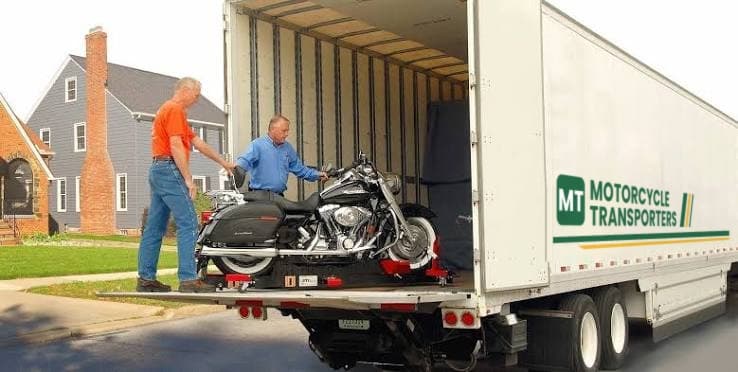 Two people loading a motorcycle into a large Motorcycle Transporters truck for door-to-door shipping in Virginia